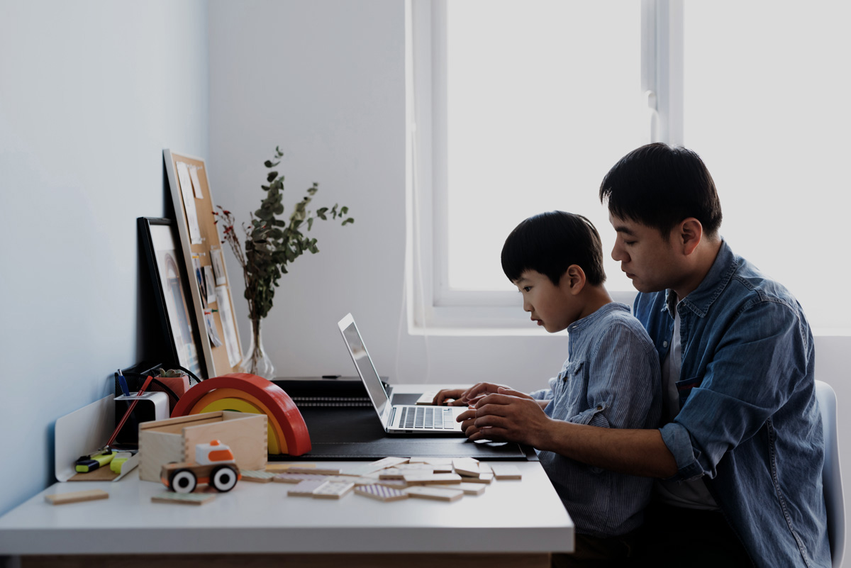 A father and young son working together on a laptop while seated at a desk