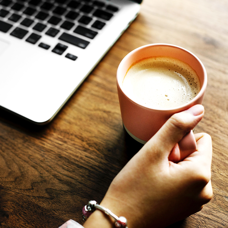 A close up image of a woman holding a coffee cup and working on her laptop