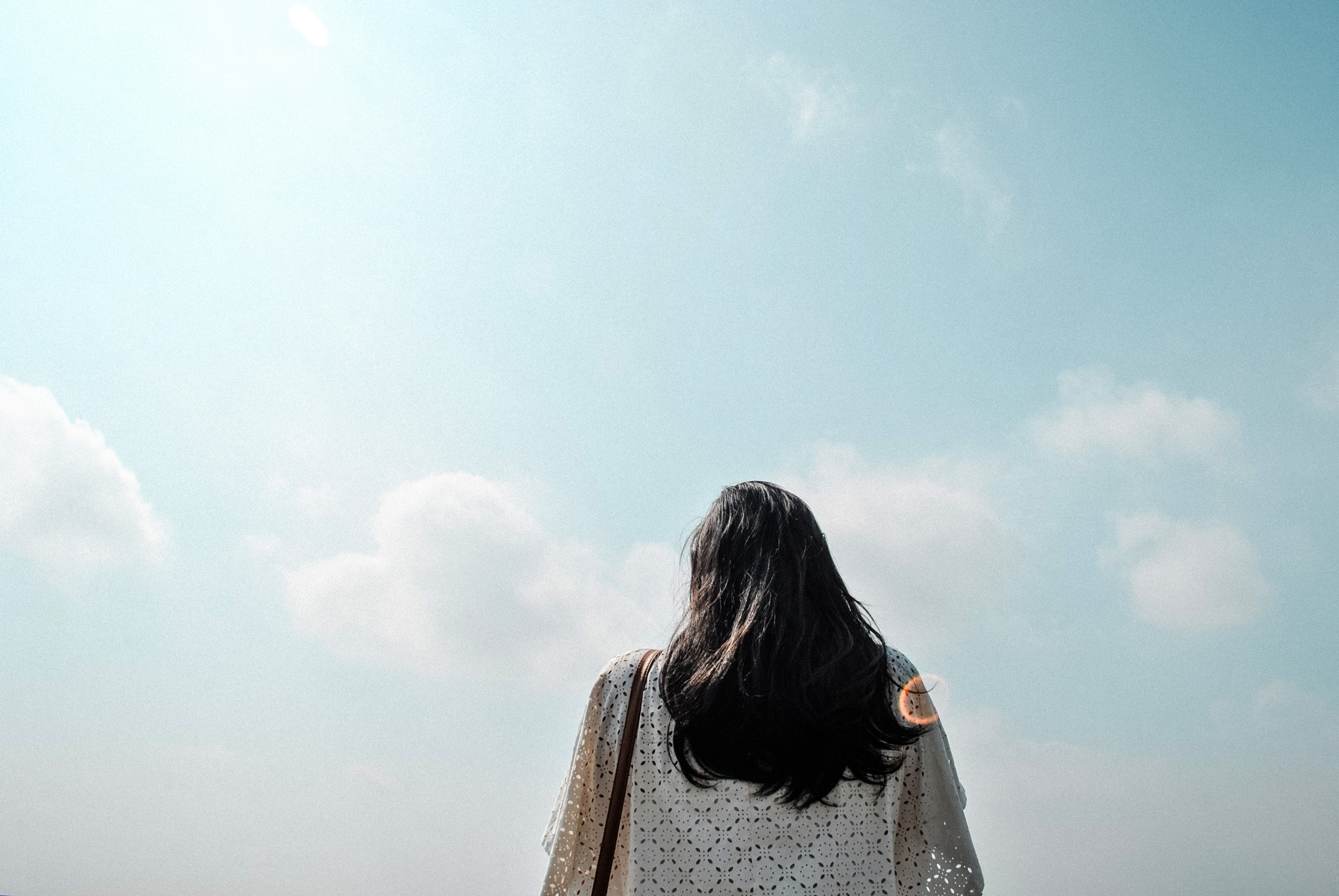 A woman looking up at the cloudy sky, which is a mix of light blue and light pink
